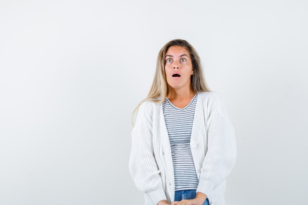 Belle femme en veste regardant et regardant surpris, vue de face.