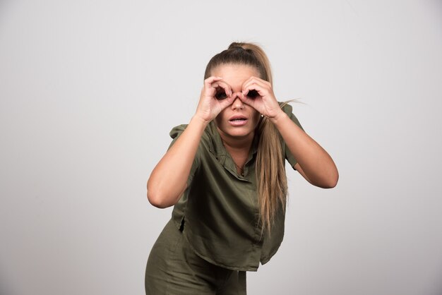 Belle femme en veste verte regardant la caméra à travers ses mains.