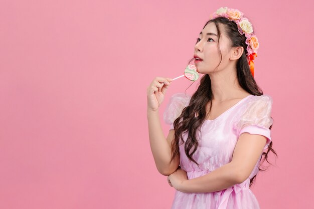 Une belle femme vêtue d'une princesse rose joue avec son bonbon sucré sur un rose.