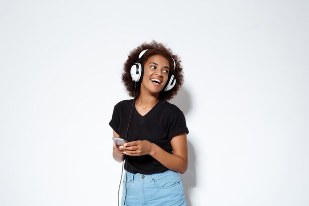 Belle fille africaine, écouter de la musique dans les écouteurs sur mur blanc