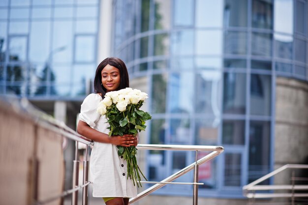 Belle fille afro-américaine tenant un bouquet de fleurs de roses blanches sur la datation dans la ville Femme d'affaires noire avec bouquet de fleurs