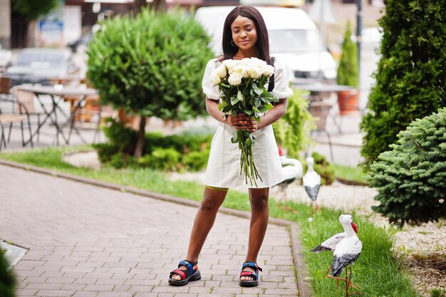 Belle fille afro-américaine tenant un bouquet de fleurs de roses blanches sur la datation dans la ville Femme d'affaires noire avec bouquet de fleurs