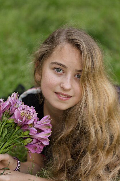 Belle fille allongée, souriant tout en tenant des fleurs à l'extérieur en t-shirt noir pendant la journée.