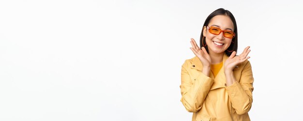 Belle fille asiatique dans des lunettes de soleil élégantes souriant heureux à la recherche de brillant et insouciant debout sur w