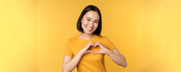 Belle fille asiatique montrant un geste d'amour du cœur et des dents blanches souriantes expriment des soins et de la sympathie st