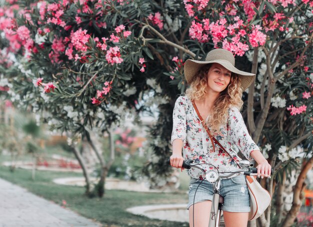 Belle fille assise sur un vélo et souriant en chemise texturée blanche pendant la journée.