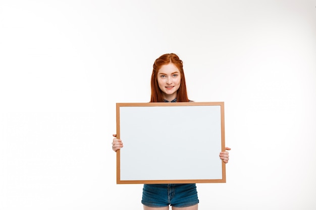 belle fille au gingembre avec tableau blanc sur mur blanc.