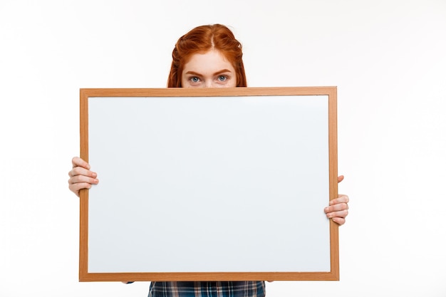 belle fille au gingembre avec tableau blanc sur mur blanc.