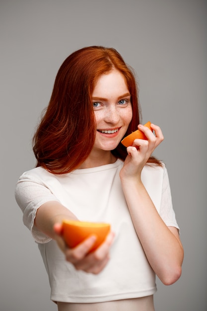 belle fille au gingembre tenant des oranges sur le mur gris.