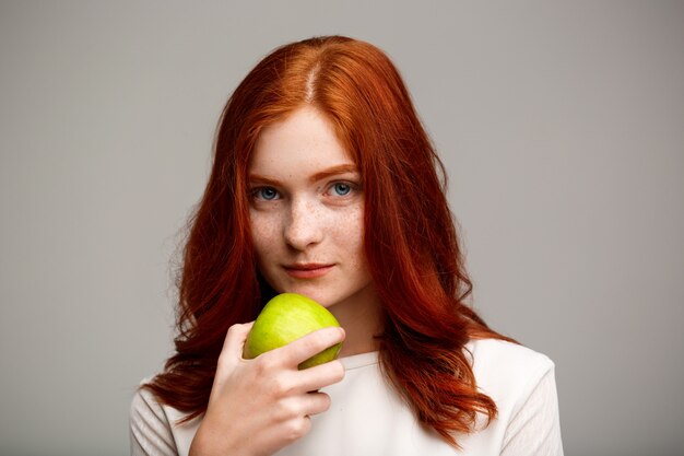 belle fille au gingembre tenant la pomme sur le mur gris.