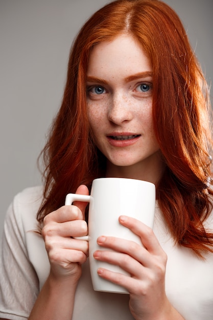 belle fille au gingembre tenant la tasse sur le mur gris.