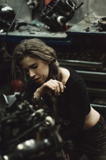 belle fille aux cheveux longs dans le garage réparer une moto