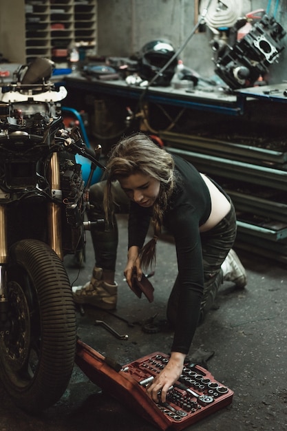 belle fille aux cheveux longs dans le garage réparer une moto