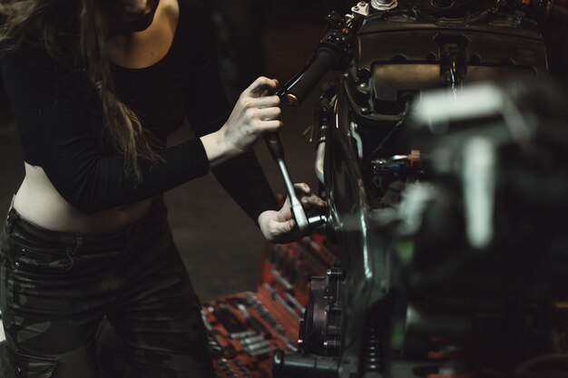 belle fille aux cheveux longs dans le garage réparer une moto