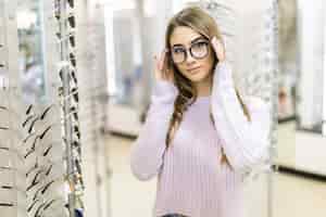 Photo gratuite belle fille aux longs cheveux dorés et au look de modèle démontre la différence de lunettes dans un magasin professionnel