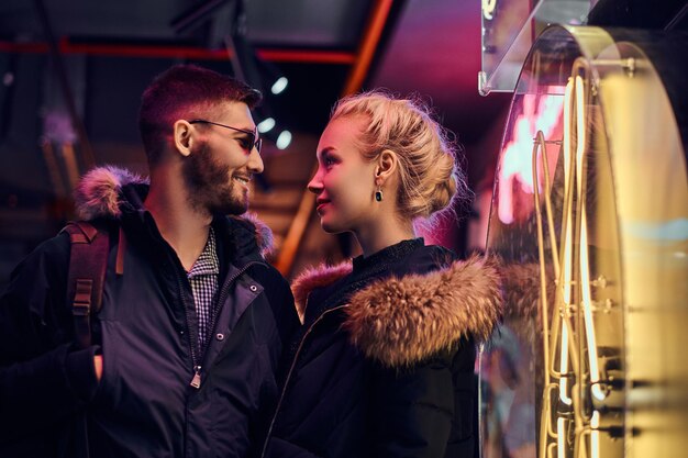 Une belle fille et bel homme debout dans la nuit dans la rue. Enseignes lumineuses, néons, luminaires.