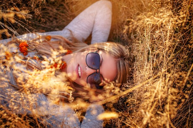 Belle fille blonde à lunettes de soleil allongée dans l'herbe jaune.