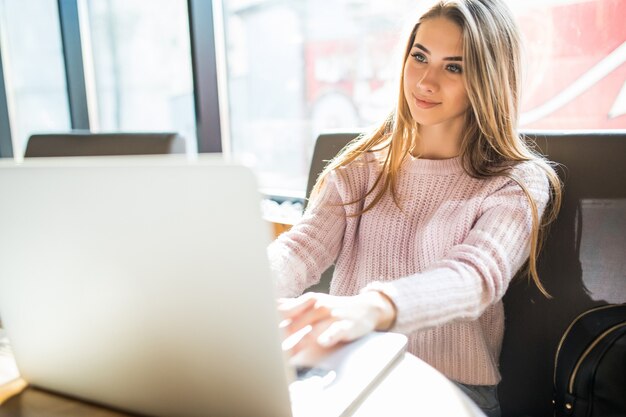 Belle fille blonde en pull blanc en travaillant sur son ordinateur portable au café dans le temps quotidien