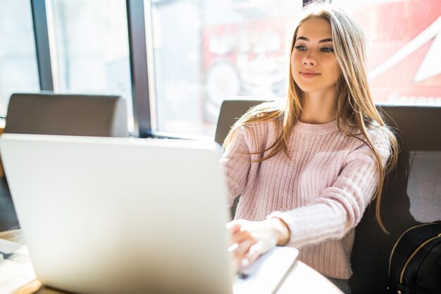 Belle fille blonde en pull de mode en travaillant sur son ordinateur portable au café dans le temps quotidien