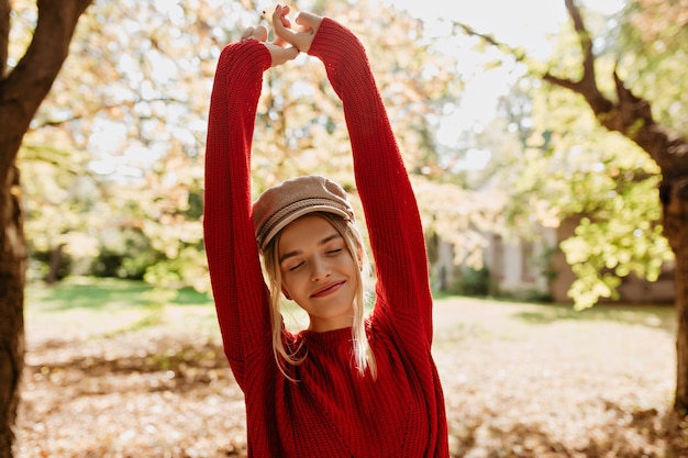 Belle fille blonde se sent heureuse dans le parc d'automne. Belle jeune femme en pull rouge posant parmi les feuilles.