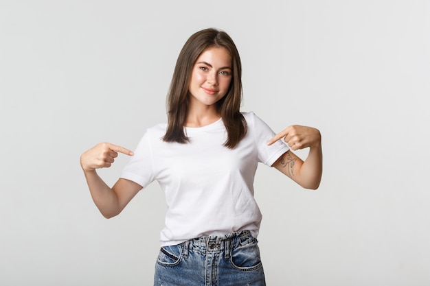 Belle fille brune souriante pointant du doigt votre logo, montrant quelque chose au centre.