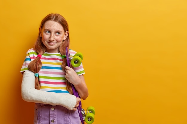 Belle fille a cassé le bras après être tombé de la planche à roulettes, aime le sport extrême, porte du plâtre, est blessée après un accident pendant l'été, espère une récupération rapide et une nouvelle conduite, isolée sur jaune