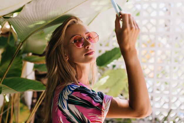 Belle fille caucasienne à lunettes de soleil roses touchant la plante verte.