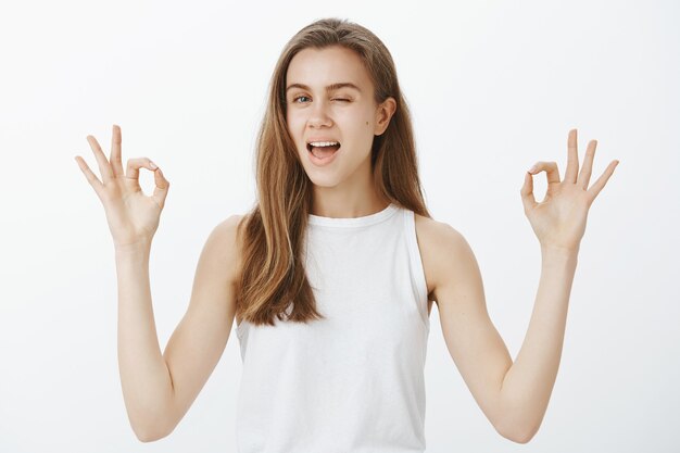 Une belle fille confiante et impertinente assure que tout va bien, montrant des gestes corrects et un clin d'œil rassurant