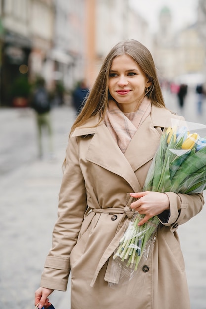 Belle Fille Dans Un Manteau Marron. Femme Dans Une Ville De Printemps. Dame Au Bouquet De Fleurs