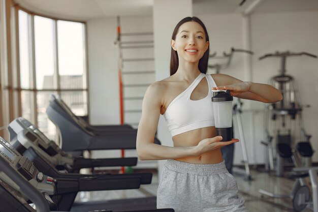 Une belle fille debout dans une salle de sport avec une bouteille d'eau