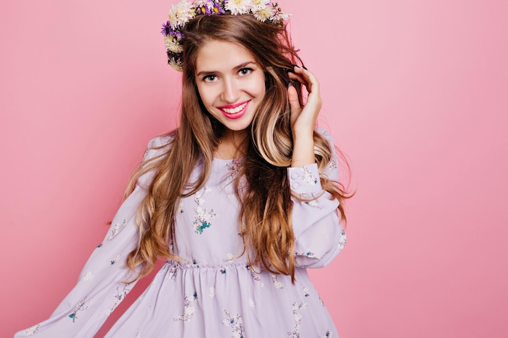 Photo gratuit belle fille européenne avec des fleurs dans les cheveux souriant sur fond rose. portrait en studio d'une jeune femme brune joyeuse avec une expression de visage heureux.