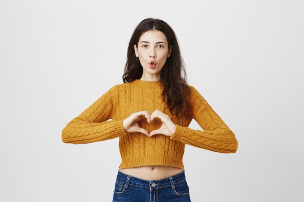 Belle fille faisant le geste du coeur et souriant, comme produit