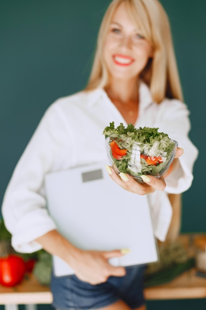 Belle fille fait une salade. Blonde sportive dans une cuisine. Femme tenant des poids dans ses mains.