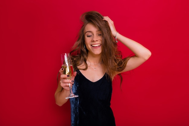 Belle fille heureuse et amicale avec de longs cheveux brun clair habillés en robe de soirée bleue buvant du champagne et les yeux fermés avec vue plaisir s'amuser et passer du temps pendant la célébration