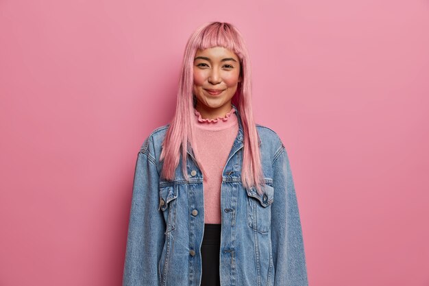 Belle fille heureuse avec de longs cheveux roses, exprime une attitude positive, porte une veste en jean à manches longues