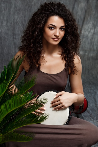 Belle fille jouant du tambour dans les plantes tropicales sur mur gris