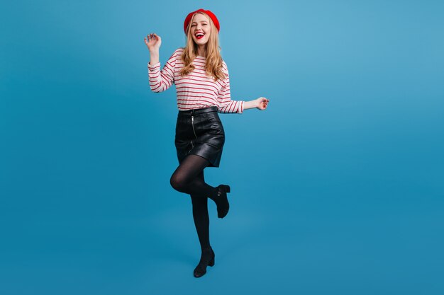 Belle fille en jupe courte dansant sur le mur bleu. Excité femme bien habillée exprimant le bonheur.