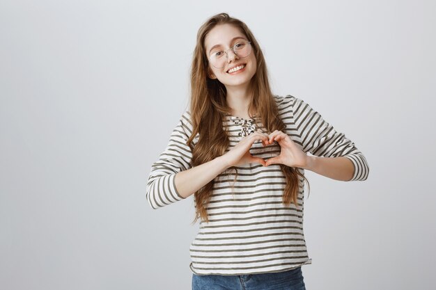 Belle fille à lunettes montrant le geste du cœur et souriant