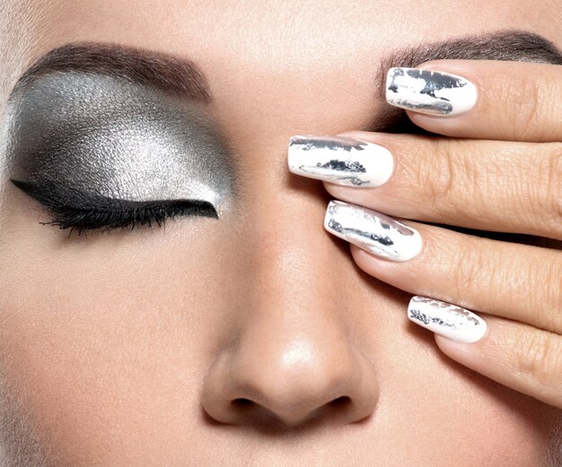 Belle fille avec le maquillage argenté et les ongles en métal.