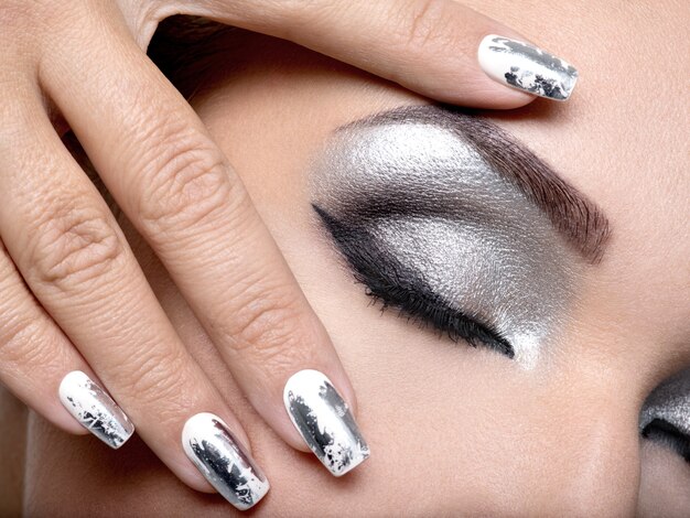 Belle fille avec le maquillage argenté des yeux et des ongles en métal.