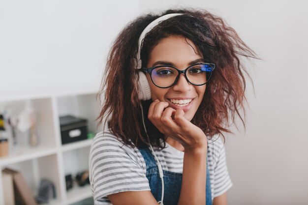 Belle fille mince avec une coiffure frisée tendance s'amuser assis à la maison et écouter de la musique