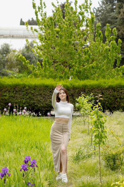 Belle fille mince debout dans le parc posant en levant la main en regardant la caméra