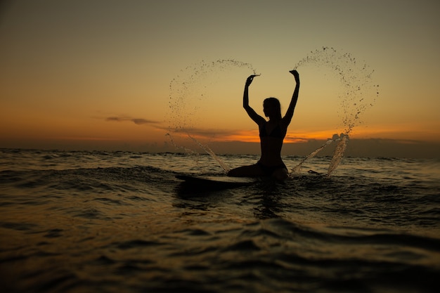 Belle fille avec une planche de surf au coucher du soleil