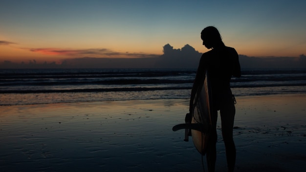 Belle fille avec une planche de surf au coucher du soleil