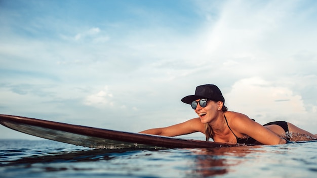 Belle fille posant assis sur une planche de surf dans l&#39;océan