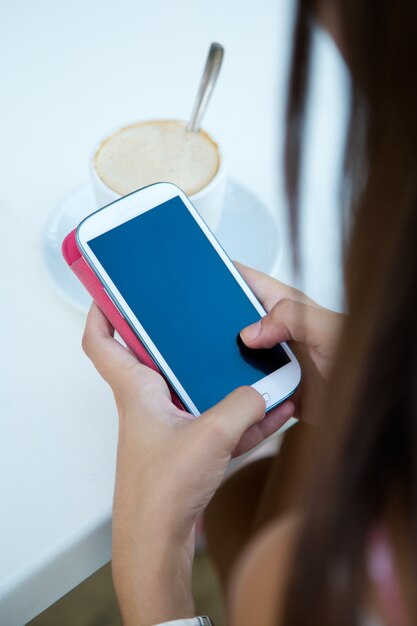 Belle fille prenant du café et des messages textuels avec un téléphone mobile.