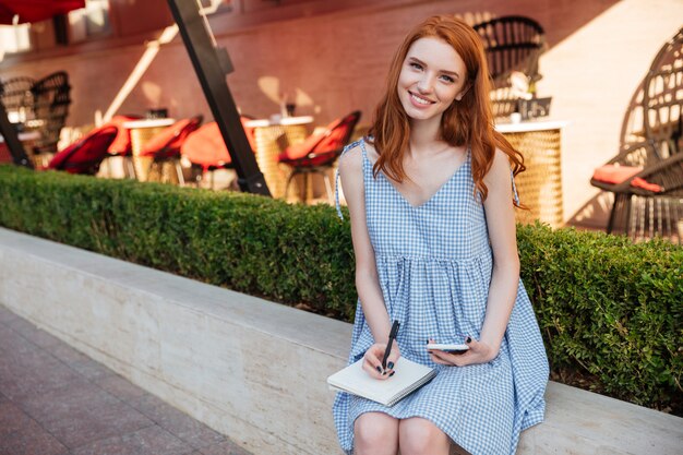 Belle fille rousse décontractée tenant un téléphone mobile