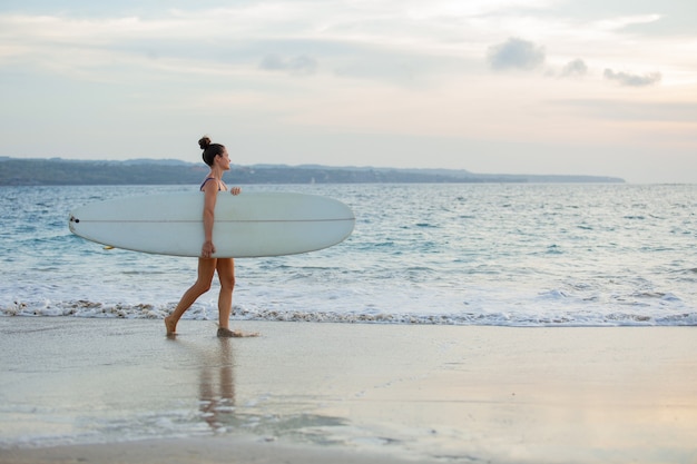 Belle fille se dresse sur la plage avec une planche de surf.