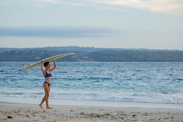 Belle fille se dresse sur la plage avec une planche de surf.