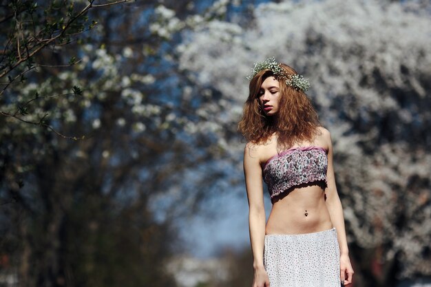 Belle fille se promène dans le jardin luxuriant vêtue d'une couronne